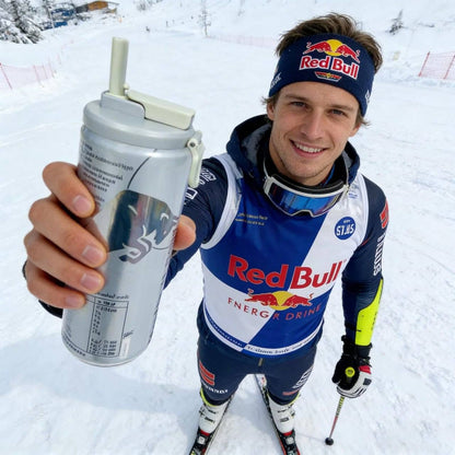 Skier holding energy drink can with reusable soda can lid and straw in snowy mountain setting